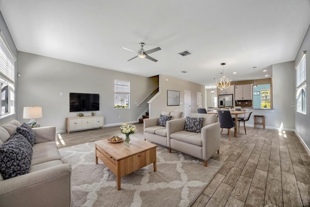 living room featuring stairway, light wood-style floors, visible vents, and a wealth of natural light