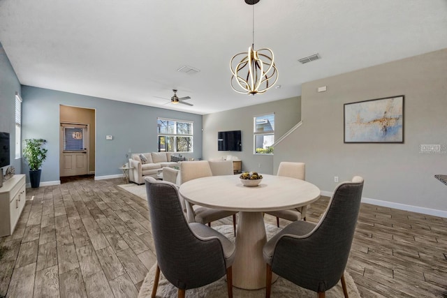 dining space featuring visible vents, ceiling fan with notable chandelier, baseboards, and wood finished floors