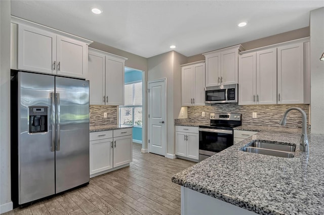 kitchen featuring light stone counters, light wood-style flooring, a sink, appliances with stainless steel finishes, and white cabinetry