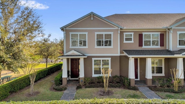 multi unit property featuring stucco siding, roof with shingles, and a front yard