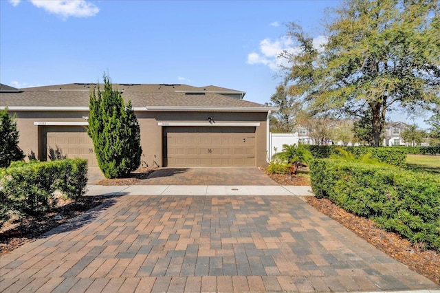 view of front facade with decorative driveway, fence, an attached garage, and stucco siding