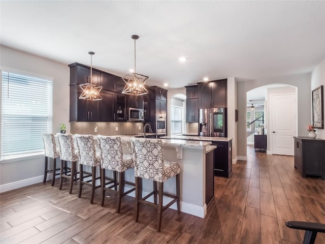 753 Daybreak Pl, Longwood, FL 32750 - kitchen featuring dark wood-style floors, a peninsula, arched walkways, decorative backsplash, and appliances with stainless steel finishes