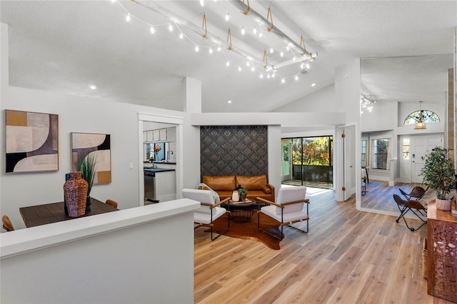 living area featuring light wood-type flooring, high vaulted ceiling, track lighting, and a textured ceiling