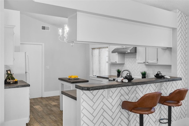 kitchen with dark countertops, visible vents, tasteful backsplash, under cabinet range hood, and a peninsula