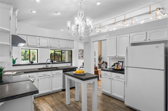 kitchen with dark countertops, dishwasher, range hood, freestanding refrigerator, and a sink