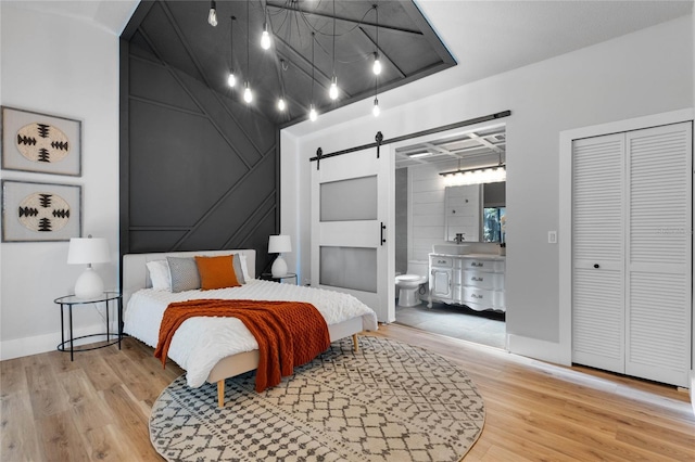 bedroom featuring baseboards, a barn door, ensuite bathroom, wood finished floors, and a closet