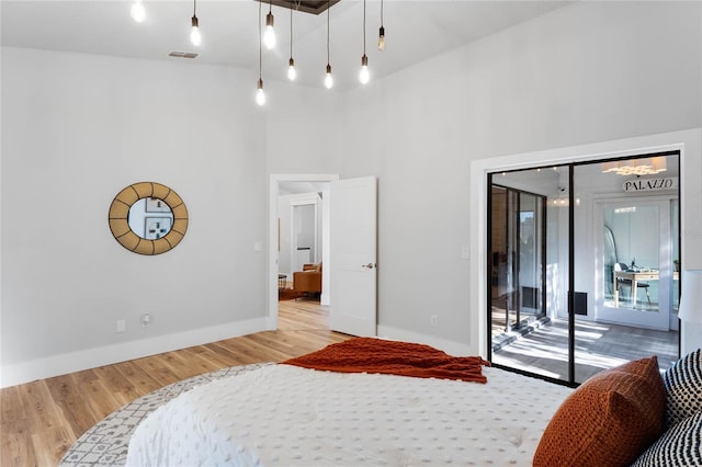 bedroom featuring visible vents, wood finished floors, a towering ceiling, baseboards, and access to exterior