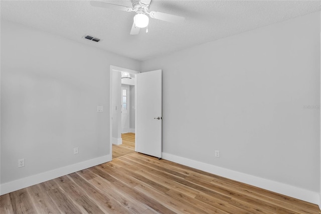 empty room featuring a ceiling fan, baseboards, visible vents, light wood-style flooring, and a textured ceiling