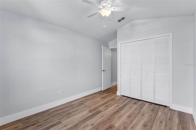 unfurnished bedroom with visible vents, baseboards, lofted ceiling, wood finished floors, and a closet