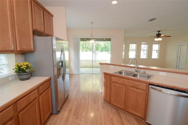 kitchen featuring light wood-type flooring, light countertops, hanging light fixtures, stainless steel appliances, and a sink