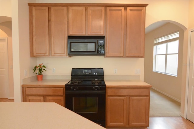 kitchen featuring arched walkways, black appliances, light countertops, and baseboards