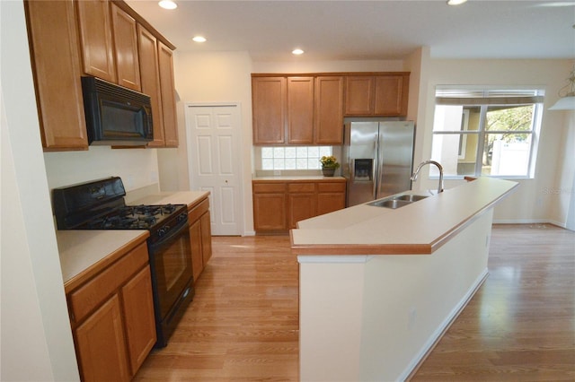 kitchen with black appliances, light wood-style flooring, a kitchen island with sink, and a sink