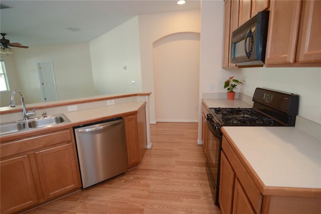 kitchen featuring light wood finished floors, ceiling fan, a sink, black appliances, and light countertops