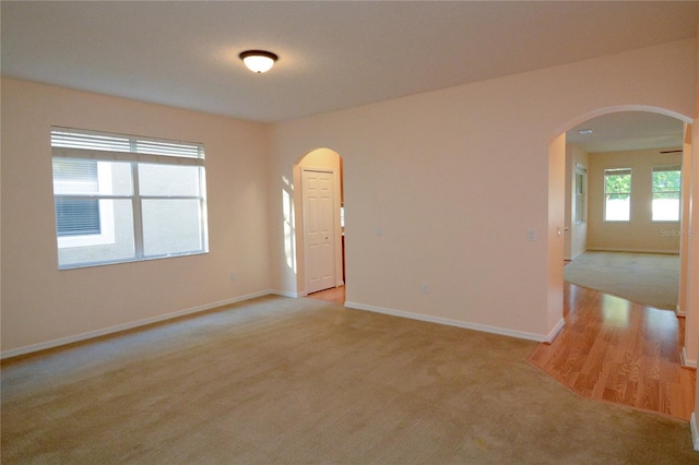 spare room with arched walkways, light colored carpet, and baseboards