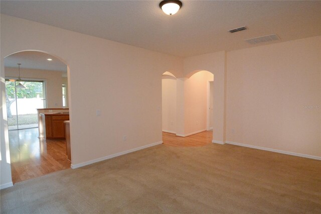 unfurnished room featuring visible vents, arched walkways, and light carpet