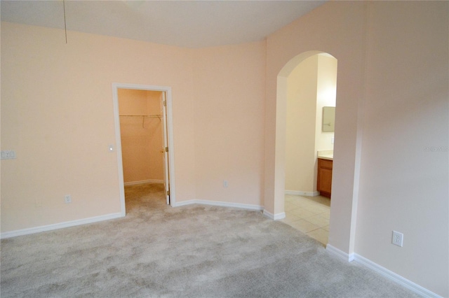 unfurnished room with arched walkways, light carpet, and baseboards