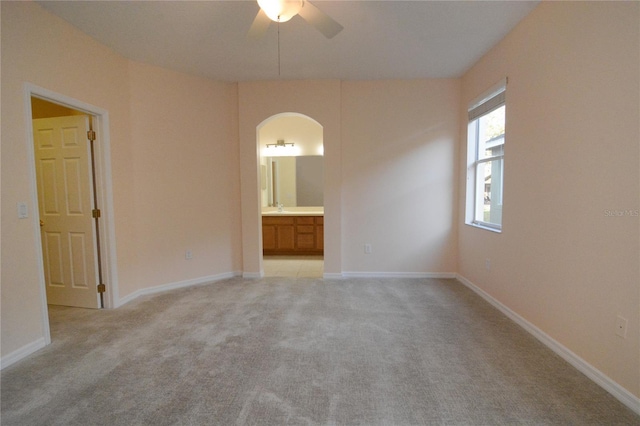 empty room featuring baseboards, a ceiling fan, arched walkways, and light carpet