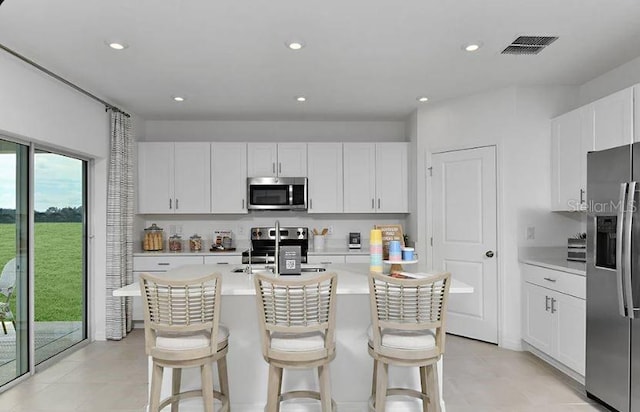 kitchen with visible vents, a center island with sink, a breakfast bar area, light countertops, and stainless steel appliances