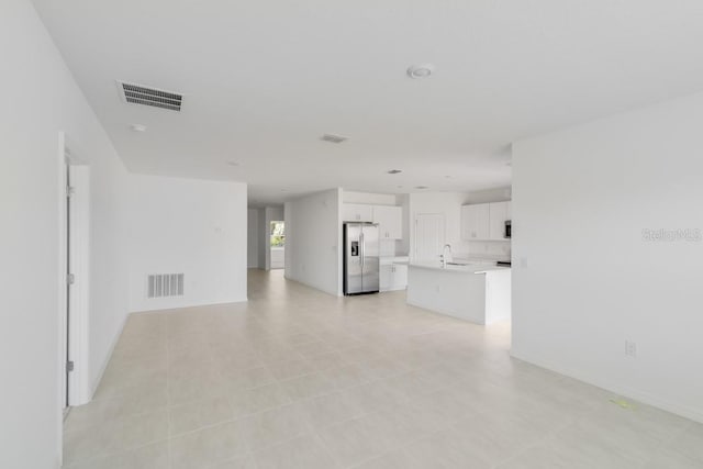 unfurnished living room with baseboards, visible vents, and a sink