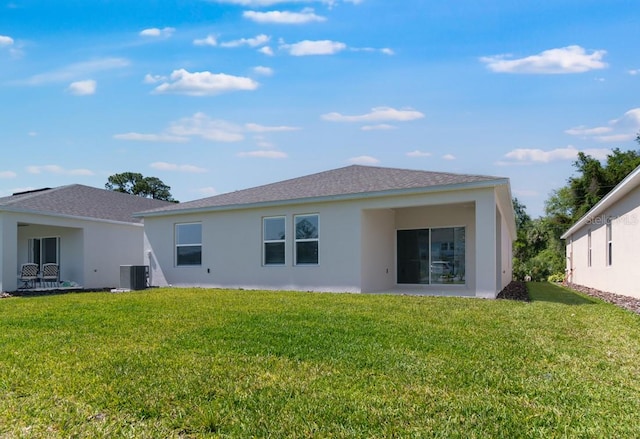 back of property with stucco siding, central AC unit, a shingled roof, and a lawn