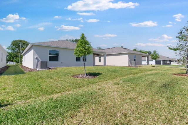 rear view of house featuring central air condition unit, a lawn, and stucco siding