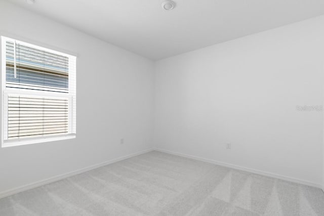 empty room featuring plenty of natural light, light carpet, and baseboards