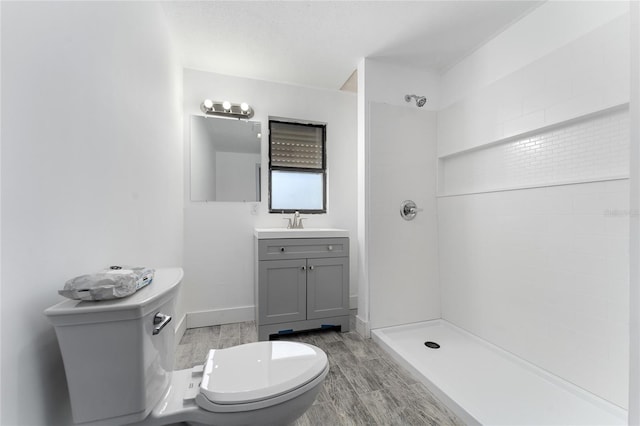 bathroom featuring tiled shower, toilet, vanity, and wood finish floors