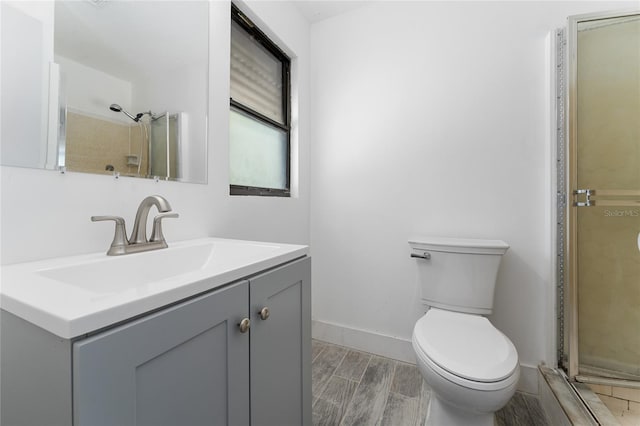 bathroom featuring wood finish floors, toilet, a shower stall, baseboards, and vanity