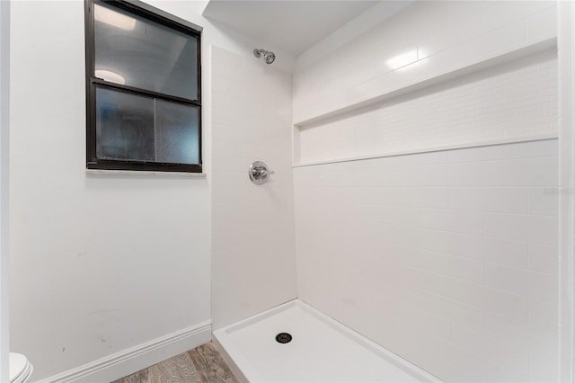 bathroom with baseboards, tiled shower, toilet, and wood finished floors