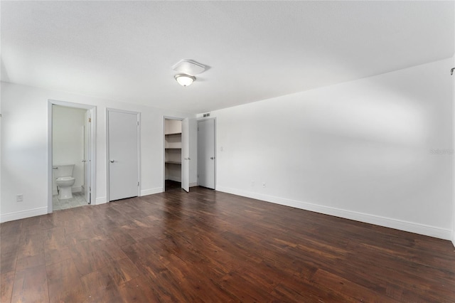 unfurnished bedroom featuring dark wood-style floors, ensuite bath, and baseboards