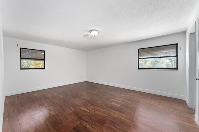 spare room with dark wood-style floors, a textured ceiling, and baseboards