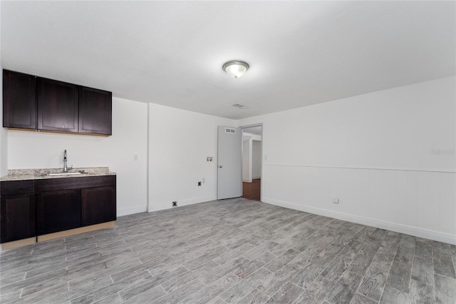 unfurnished living room with indoor wet bar, light wood-style floors, visible vents, and a sink