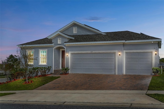 ranch-style home with stucco siding, an attached garage, a shingled roof, and decorative driveway