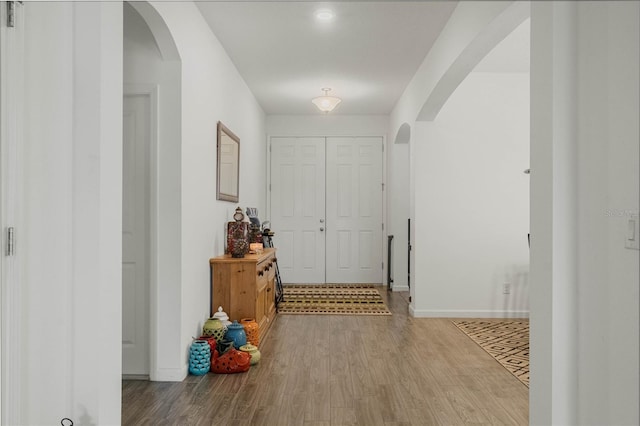 foyer entrance with arched walkways, baseboards, and wood finished floors