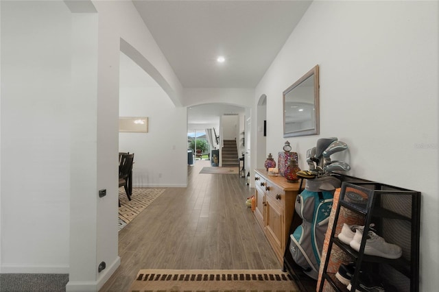 hall with arched walkways, baseboards, and wood finished floors