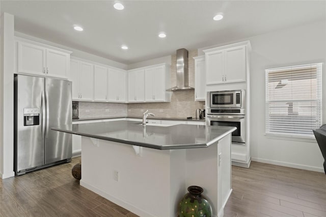 kitchen featuring dark wood-type flooring, wall chimney range hood, backsplash, and stainless steel appliances