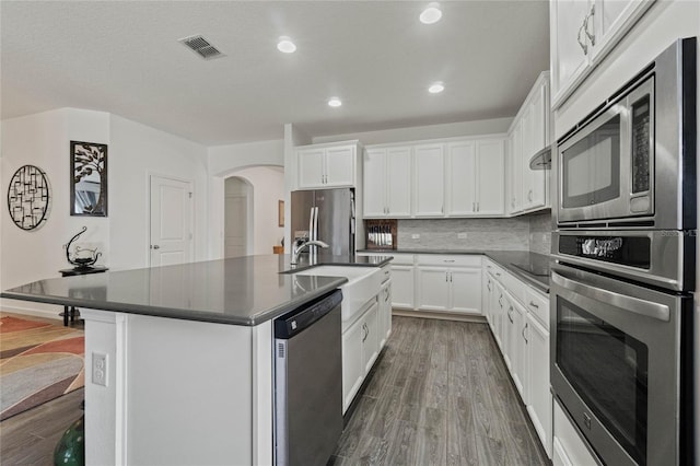 kitchen featuring dark countertops, backsplash, appliances with stainless steel finishes, wood finished floors, and arched walkways