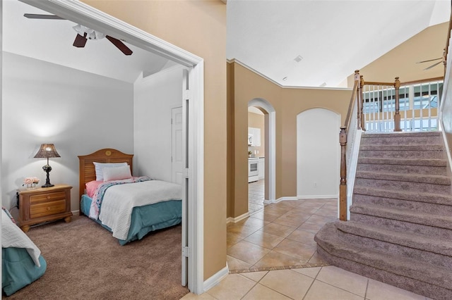 bedroom with baseboards, vaulted ceiling, light tile patterned floors, arched walkways, and a ceiling fan