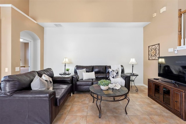 living room with light tile patterned floors, visible vents, arched walkways, and a towering ceiling