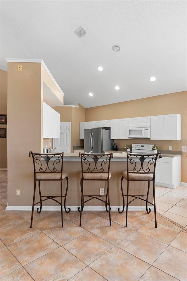 kitchen with visible vents, a kitchen breakfast bar, electric range oven, freestanding refrigerator, and white microwave