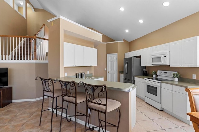 kitchen with white appliances, light tile patterned floors, a breakfast bar, vaulted ceiling, and white cabinets