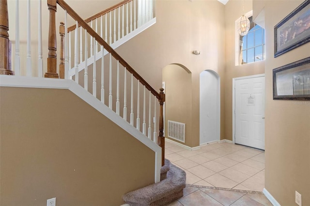 entryway featuring baseboards, visible vents, stairs, tile patterned flooring, and a towering ceiling