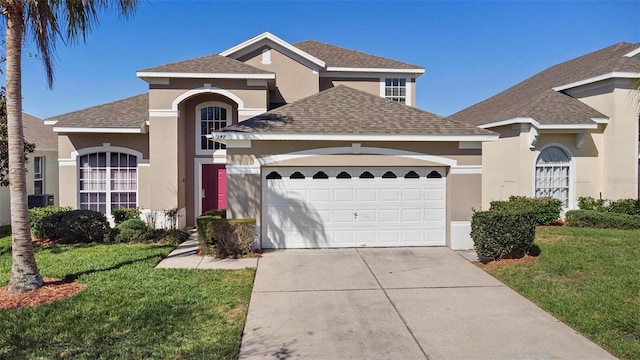 traditional home featuring stucco siding, driveway, roof with shingles, a front yard, and a garage