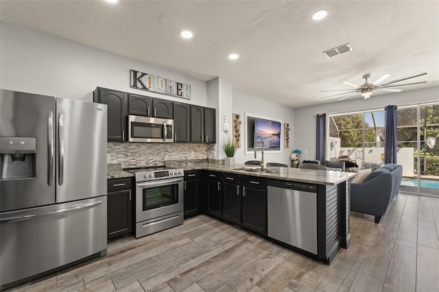 kitchen featuring stone counters, stainless steel appliances, visible vents, and light wood finished floors