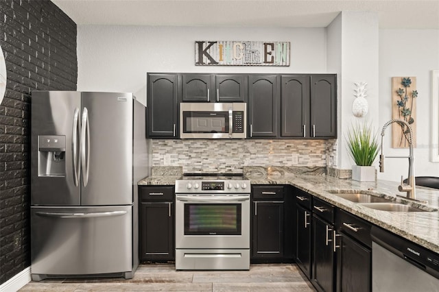 kitchen with light stone counters, light wood-style flooring, a sink, decorative backsplash, and stainless steel appliances