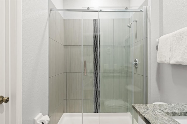 full bath with toilet, a stall shower, vanity, and a textured wall