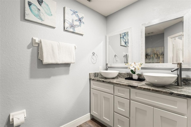 full bathroom featuring double vanity, wood finished floors, baseboards, and a sink