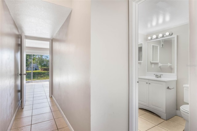 corridor with a textured ceiling, light tile patterned floors, baseboards, and a sink