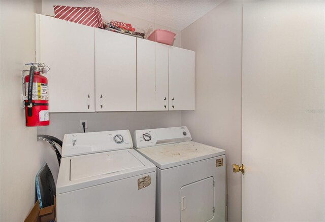 washroom featuring cabinet space, a textured ceiling, and washing machine and clothes dryer