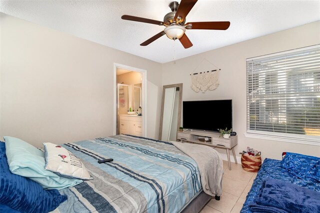 bedroom featuring a textured ceiling, ensuite bath, light tile patterned floors, baseboards, and ceiling fan